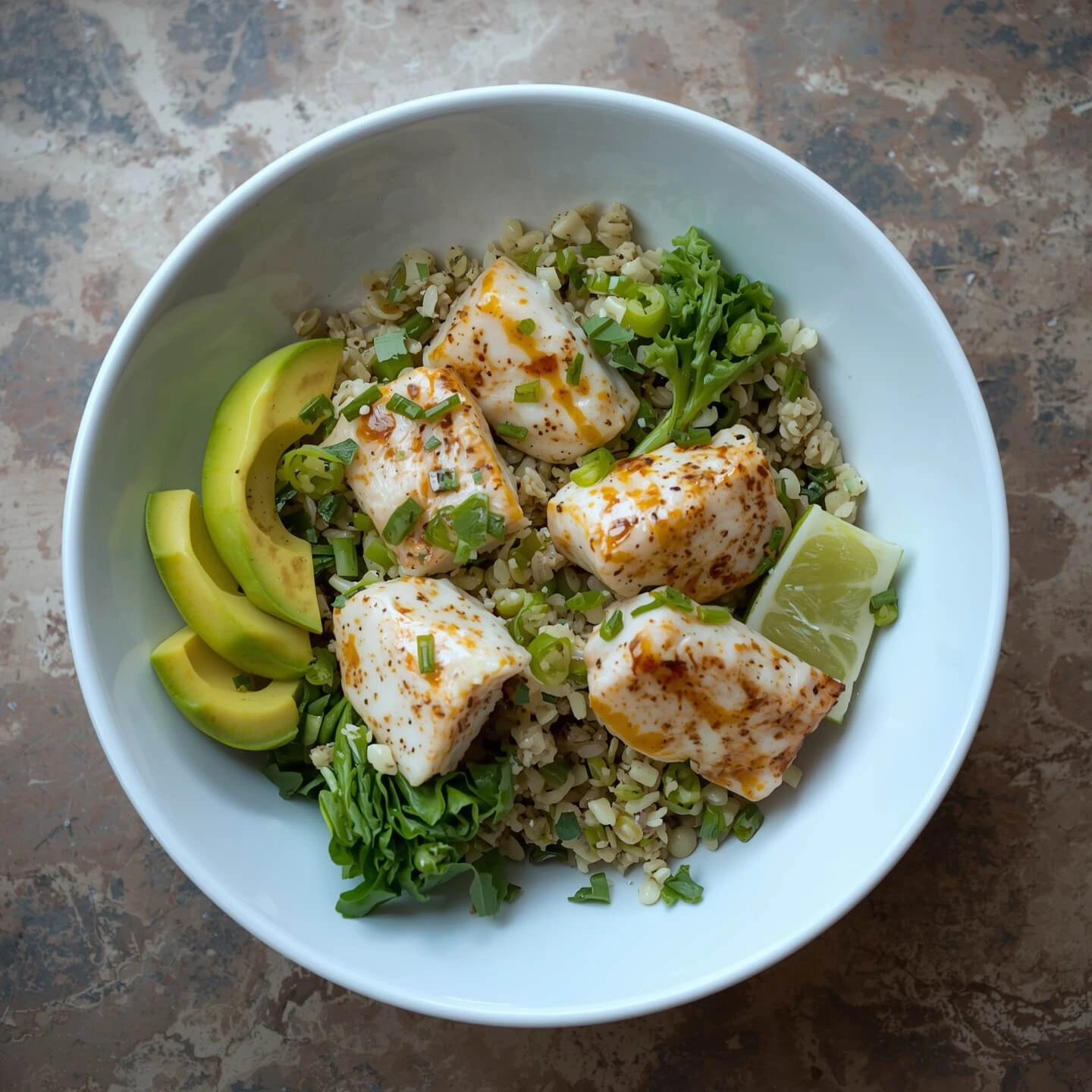 A bowl of grilled fish fillets on a bed of rice, with avocado slices, lime wedges, and fresh greens, topped with chopped green onions.