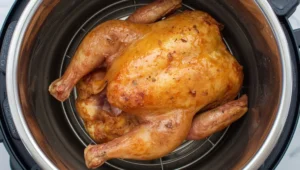 Whole cooked chicken inside an Instant Pot, showing a moist golden skin with seasoning.