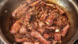 Sliced Korean beef ribs in a glossy glaze with sesame seeds and fresh green onions over white rice