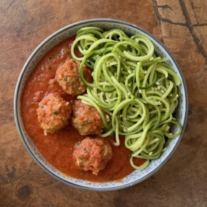 Ground chicken meatballs in marinara sauce served with zucchini noodles, garnished with fresh herbs.