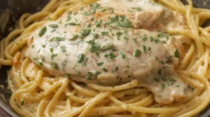Close-up of chicken carbonara with creamy sauce and spaghetti, garnished with parsley and cracked pepper.